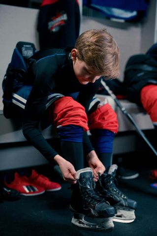 Teen boy ties hockey skates in locker room, preparing for a game.