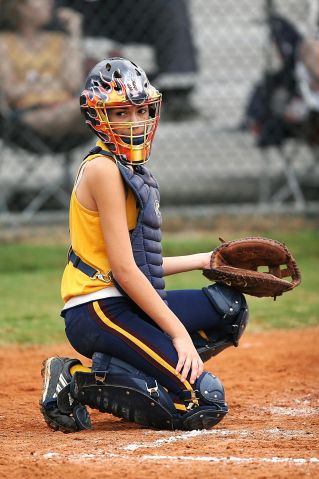 Young female softball catcher in full gear ready in a crouch position on the field.